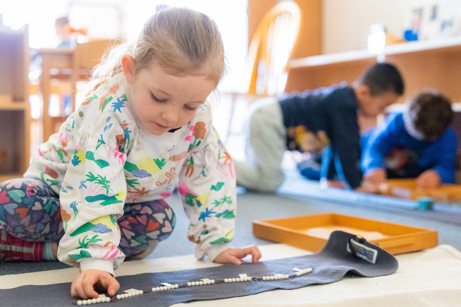 young girl in a multi-colored sweatshirt moves white beads on a gray rug