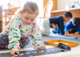 young girl in a multi-colored sweatshirt moves white beads on a gray rug