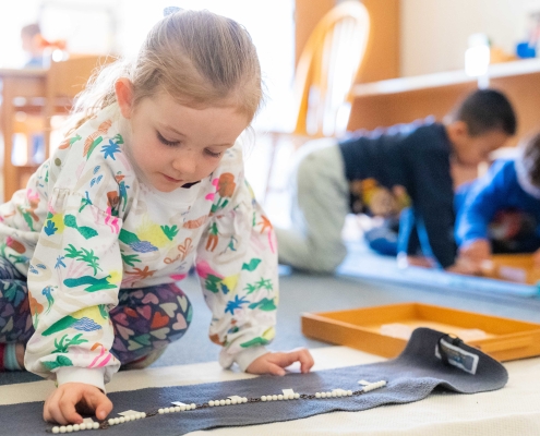 young girl in a multi-colored sweatshirt moves white beads on a gray rug